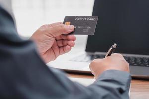 Businessman make online banking, making a payment or purchasing on the internet entering his credit card details on a smartphone and use laptop working on table photo