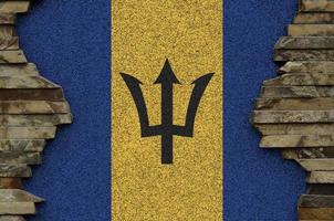 Barbados flag depicted in paint colors on old stone wall closeup. Textured banner on rock wall background photo