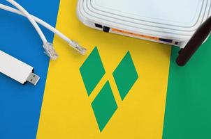 Saint Vincent and the Grenadines flag depicted on table with internet rj45 cable, wireless usb wifi adapter and router. Internet connection concept photo