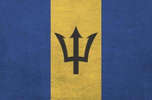 Barbados flag depicted in bright paint colors on old relief plastering wall. Textured banner on rough background photo