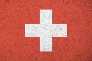 Switzerland flag depicted in bright paint colors on old relief plastering wall. Textured banner on rough background photo