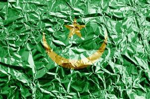 Mauritania flag depicted in paint colors on shiny crumpled aluminium foil closeup. Textured banner on rough background photo