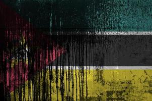 Mozambique flag depicted in paint colors on old and dirty oil barrel wall closeup. Textured banner on rough background photo