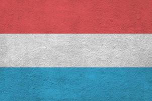 Luxembourg flag depicted in bright paint colors on old relief plastering wall. Textured banner on rough background photo