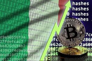 bandera de italia y flecha verde ascendente en la pantalla de minería de bitcoin y dos bitcoins dorados físicos foto