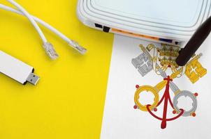 Vatican City State flag depicted on table with internet rj45 cable, wireless usb wifi adapter and router. Internet connection concept photo