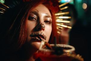 mujer con maquillaje de esqueleto en una fiesta de halloween bebe un cóctel. foto