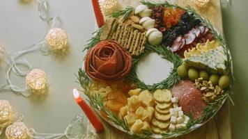 plato de charcutería con salami, diferentes tipos de queso. tiene frutos secos, frutos secos varios y miel. arreglo de vacaciones con velas encendidas video