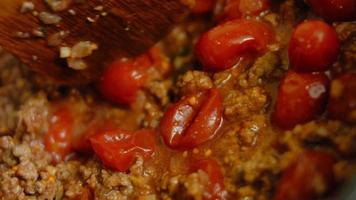 mengen de ingrediënten voor de chorizo en de bewaard gebleven tomaten met een houten lepel. macro het schieten video