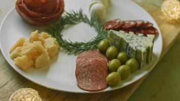 charcutaria plana com salame, diferentes tipos de queijo. tem frutas secas, nozes diversas e mel. arranjo de férias com velas acesas video