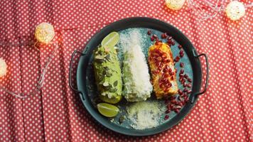 Mexicaans maïs Elote in drie manieren. ingedrukt met kaas, guacamole en granaatappel. maxicaans vlag video