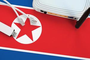 bandera de corea del norte representada en la mesa con cable de internet rj45, adaptador wifi usb inalámbrico y enrutador. concepto de conexión a internet foto