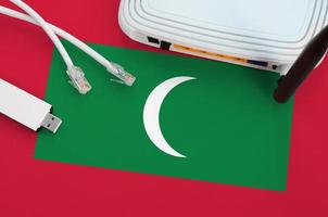 bandera de maldivas representada en la mesa con cable de internet rj45, adaptador wifi usb inalámbrico y enrutador. concepto de conexión a internet foto