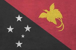 Papua New Guinea flag depicted in bright paint colors on old relief plastering wall. Textured banner on rough background photo