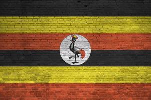 Uganda flag depicted in paint colors on old brick wall. Textured banner on big brick wall masonry background photo