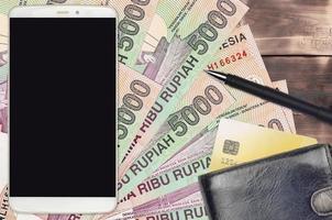 Billetes de 5000 rupias indonesias y smartphone con monedero y tarjeta de crédito. pagos electrónicos o concepto de comercio electrónico. compras y negocios en línea con dispositivos portátiles foto