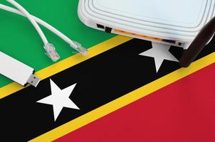 bandera de saint kitts y nevis representada en la mesa con cable de internet rj45, adaptador wifi usb inalámbrico y enrutador. concepto de conexión a internet foto