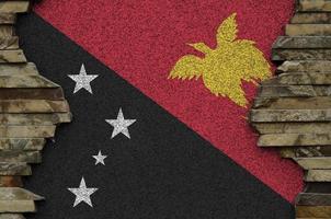 bandera de papua nueva guinea representada en colores de pintura en el primer plano de la pared de piedra antigua. banner texturizado sobre fondo de pared de roca foto