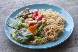 Fried noodle with pork, chinese kale and carrot thai call Rad Na in blue plate on wooden table. photo