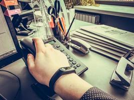 a man in a blue shirt with a pattern picks up a black phone to make a call. the guy has a fitness bracelet on his arm. call on a landline, city phone. retro telephone with buttons photo
