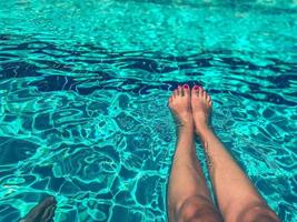 pies de una chica con una pedicura brillante en la piscina. nadar en el agua en un país cálido y tropical. piernas delgadas en la piscina foto