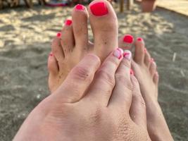 Female legs, feet with a beautiful red pedicure on the background of sand on vacation on the beach in a warm tropical eastern paradise country southern resort photo