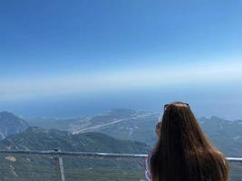 Mature female traveler looks through tourist binocular at mountains and sea. Concept of traveling for retired persons photo