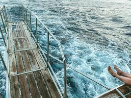 bridge made of wood with metal breaks into the sea. water with waves and white foam. bridge on a yacht for swimming and jumping. a tourist is sitting on the bridge photo