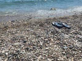 chanclas azules en la playa de guijarros con mar turquesa y cielo azul de fondo. Hora de verano. concepto de vacaciones foto