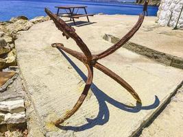 ancla vieja y oxidada en la orilla del mar. en el puerto con barcos y yates hay un ancla. los turistas pueden ver óxido anclado. tapón marino en óxido, óxido de agua foto