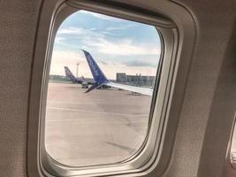 una pequeña ventana de vidrio templado a bordo de un avión. los pasajeros miran al suelo desde su asiento. la cola del avión es visible en la ventana foto