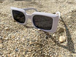 gafas de sol de plástico blanco para mujeres en la arena amarilla de una playa en un cálido paraíso tropical del este del país resort foto