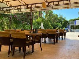 restaurante al aire libre con mesas y sillas en el espacio abierto bajo las palmeras frente al mar azul tranquilo y la playa de arena. copie el espacio foto