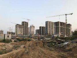 tall houses in the city center. houses are being built with a crane, the crane is carrying heavy concrete blocks. there are many glass panoramic windows in the houses photo