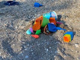 juguetes para niños para jugar en los cubos de la caja de arena y moldes con palas en una playa de guijarros cerca del mar foto