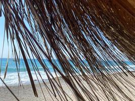 View of the blue sea with salt water through the yellow dry straw of the sun umbrella on the beach in the warm eastern tropical country southern paradise resort. The background photo