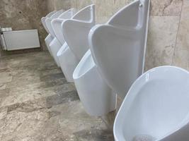 fila de urinarios blancos en un baño público foto