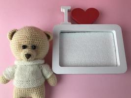 soft knitted bear on a pink background with a cute frame in white. a bear with black eyes made of beads lies and looks at a photograph photo
