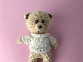 soft knitted bear on a pink matte background. bear for a gift, a toy for children. interesting interior bear, stylish bear made of threads photo