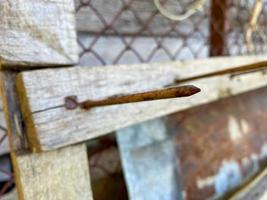 A large long rusty old iron metal construction industrial nail sticks out of a wooden plank photo