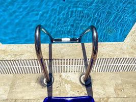 vacaciones junto al mar junto a la piscina. piscina profunda con agua clara y azul con lejía en el interior. escalera de metal para descender a la piscina, nadar en el agua foto