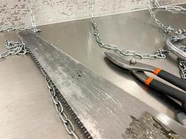 Large iron sharp metal scissors, metal cutters and a saw with chains lie on an iron table. Hand-held locksmith tools. The background photo