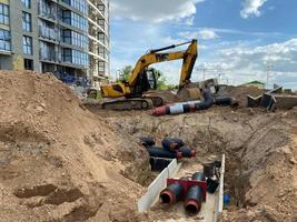 Powerful yellow industrial professional excavator doing earthwork underground repair work and burying large black water pipes at a construction site photo