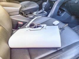 White women's beautiful fashionable leather bag and sunglasses with wireless headphones lie on the leather armchair of a good expensive car photo