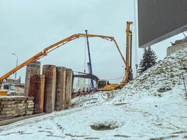 construcción de un puente en el centro de la ciudad en invierno bajo la nieve. máquinas para la construcción de grandes estructuras y barreras de hormigón foto