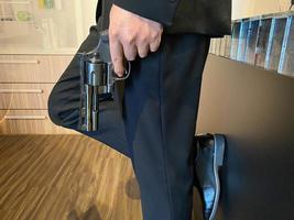 Close up on hand of unknown caucasian man holding a gun in by his leg while standing outdoor in sunny day - handgun criminal or self-defense concept with copy space photo