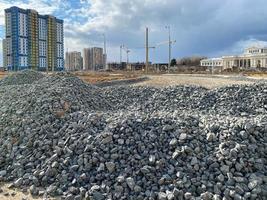 Large gray stones, rubble from industrial road construction and a view of new buildings with cranes at the construction site photo