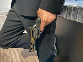 Close up on hand of unknown caucasian man holding a gun in by his leg while standing outdoor in sunny day - handgun criminal or self-defense concept with copy space photo