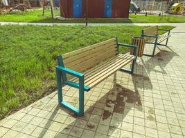 wooden benches in the park. a place for recreation for city residents, unity with nature. outdoor time near greenery and water. next to a trash bin made of wood and a playground photo