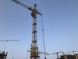 construction crane on a background of blue sky. a yellow, metal, heavy-duty crane transports concrete blocks to a height for the construction of a multi-storey building photo